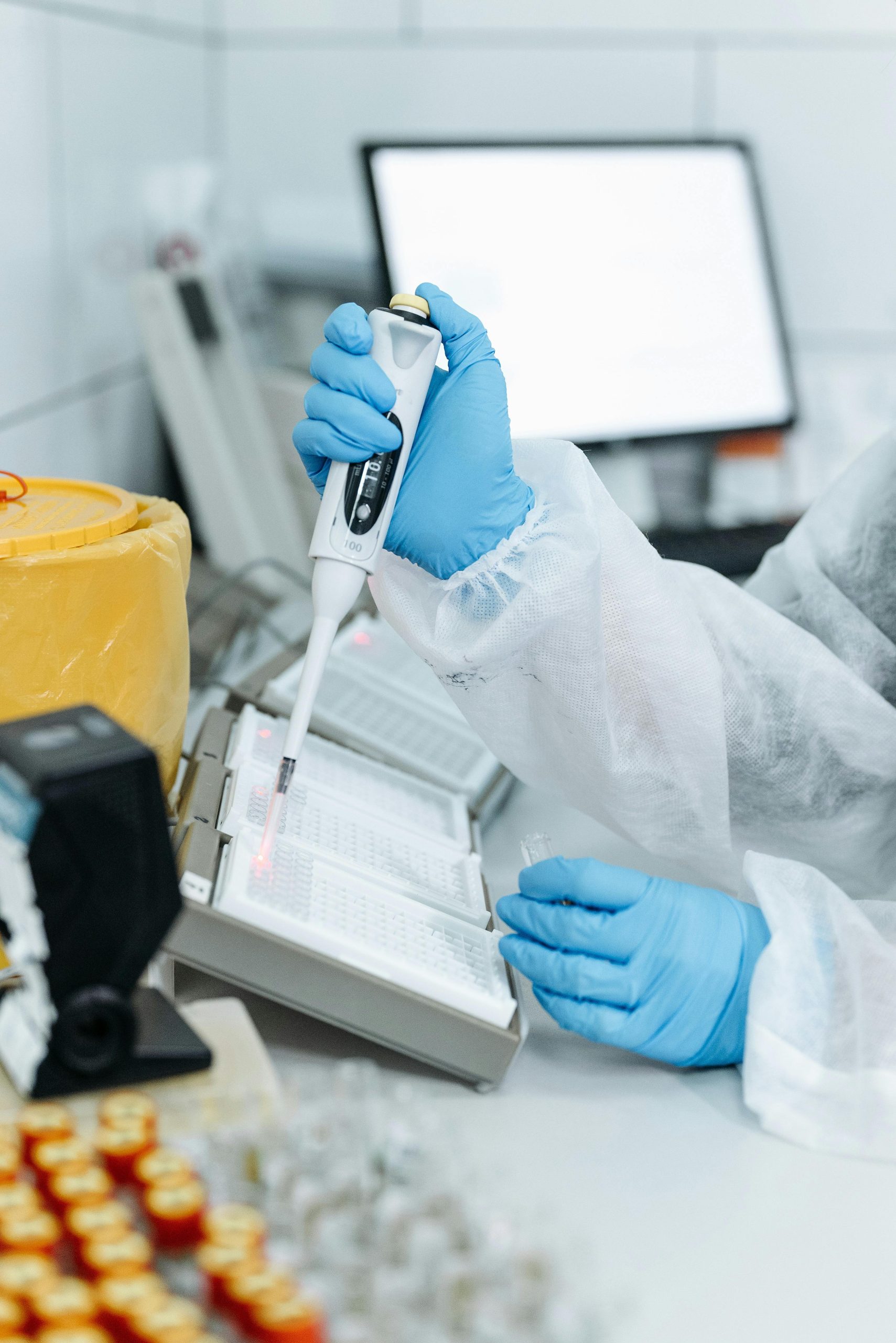 Professional in protective gear using a pipette in a laboratory setting with advanced equipment.
